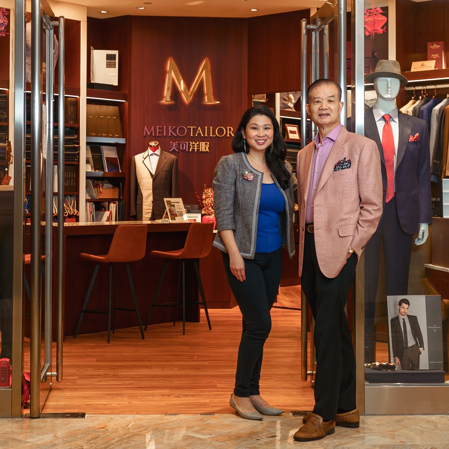 A woman and a man standing in front of Meiko Tailor's store
